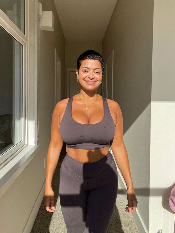 Mulher de cabelo curto, em roupa de ginástica, caminhando pelo corredor de casa com luz do sol